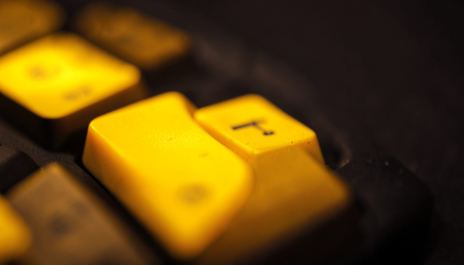 Close-up of keyboard keys in soft focus, warm amber backlight glow, dark charcoal background