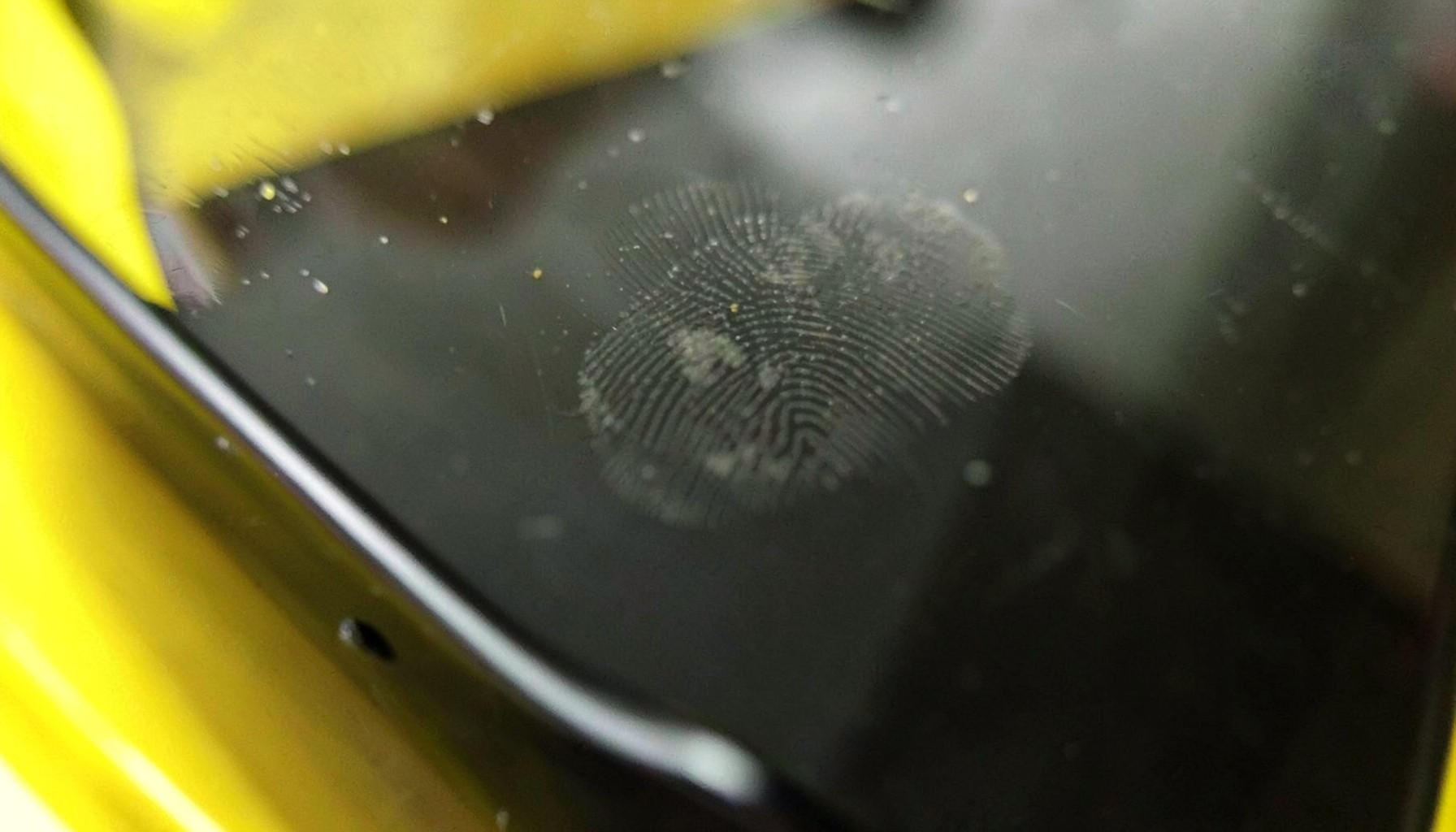 Extreme close-up of smartphone screen glass with subtle fingerprint smudges, dark reflective surface