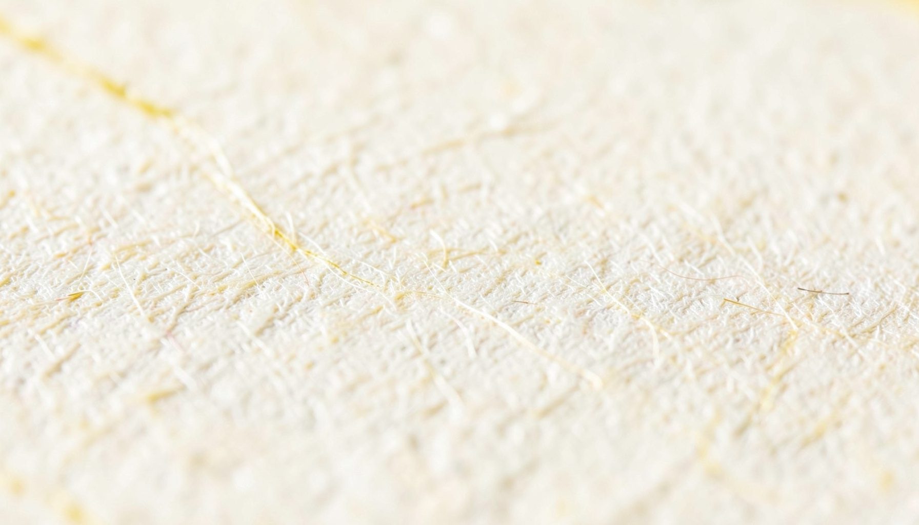Extreme close-up photograph of textured off-white paper with subtle fiber strands and a soft warm cream tone, conveying a tactile writing surface.
