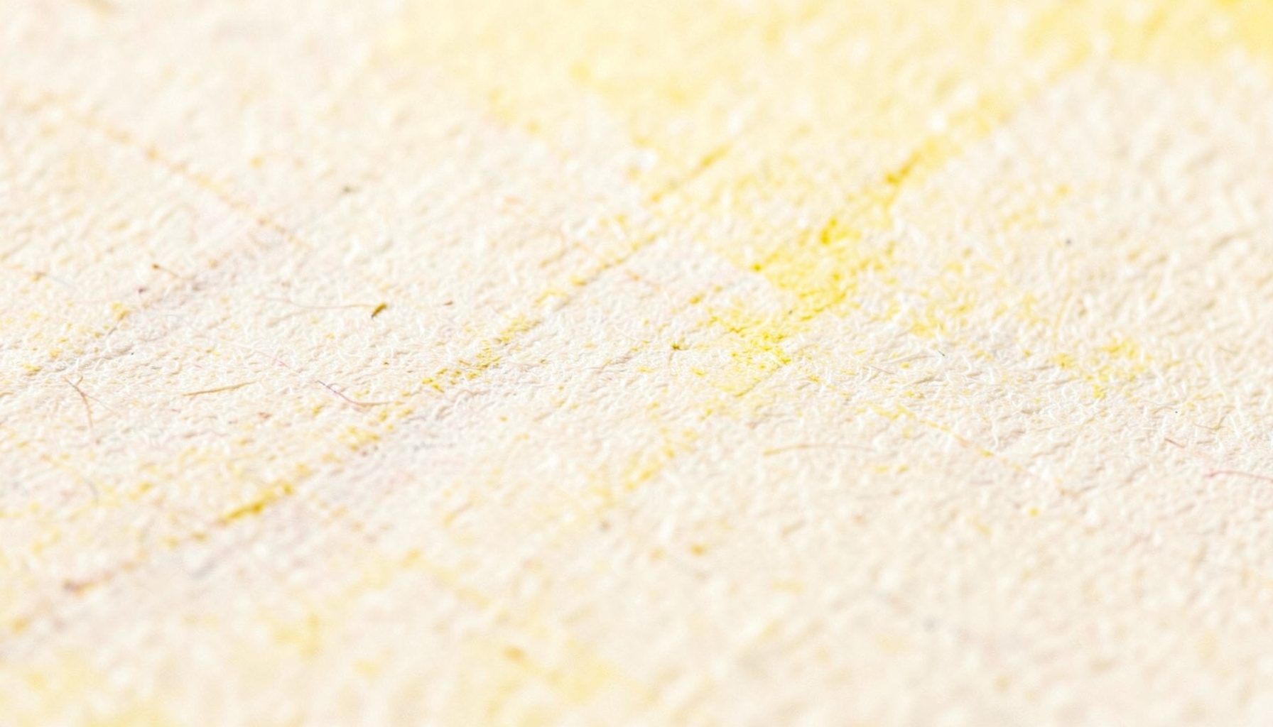 Extreme close-up photograph of matte newsprint paper with subtle fiber texture, warm off-white tones, and faint ink impressions.