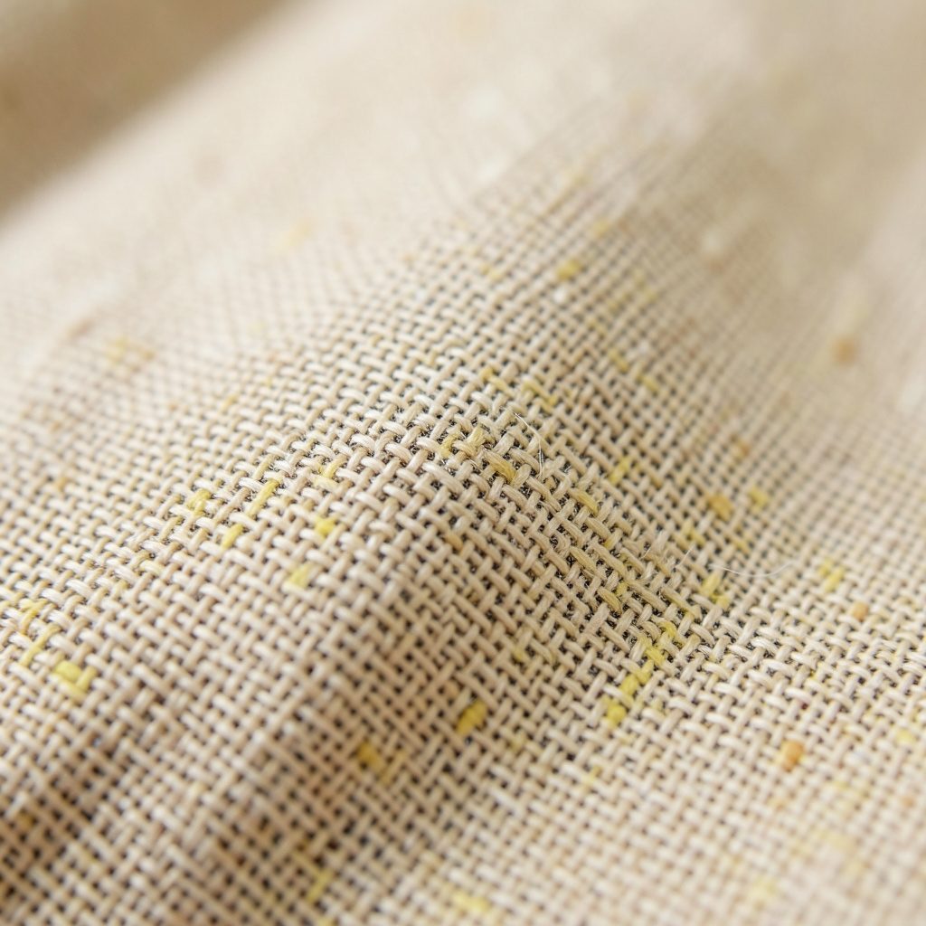 Close-up of woven linen fabric in natural beige, showing fine thread detail and organic texture